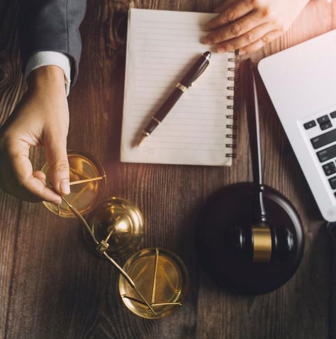 A Person is Holding a Scale of Justice Next to a Notebook and a Laptop — Olympus Lawyers In Ballarat Central, VIC