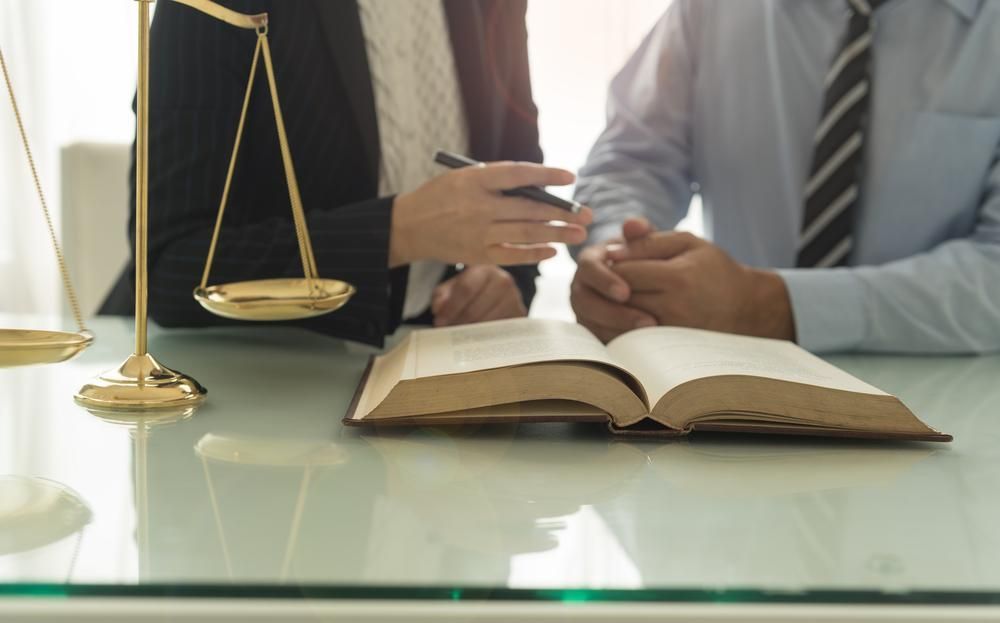 A Man and a Woman Are Sitting at a Table With a Book and Scales of Justice — Olympus Lawyers In Ballarat Central, VIC