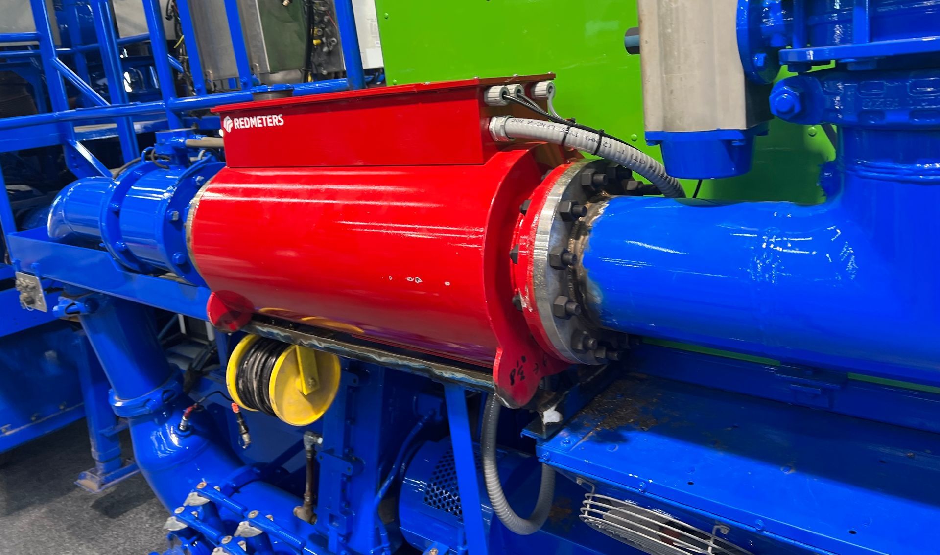 Red and blue industrial machinery components, including a red cylindrical device, blue pipes, and a green background.