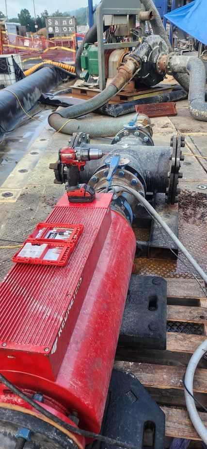 A red industrial machine with a toolkit on top is connected to pipes and hoses, likely on a construction site.