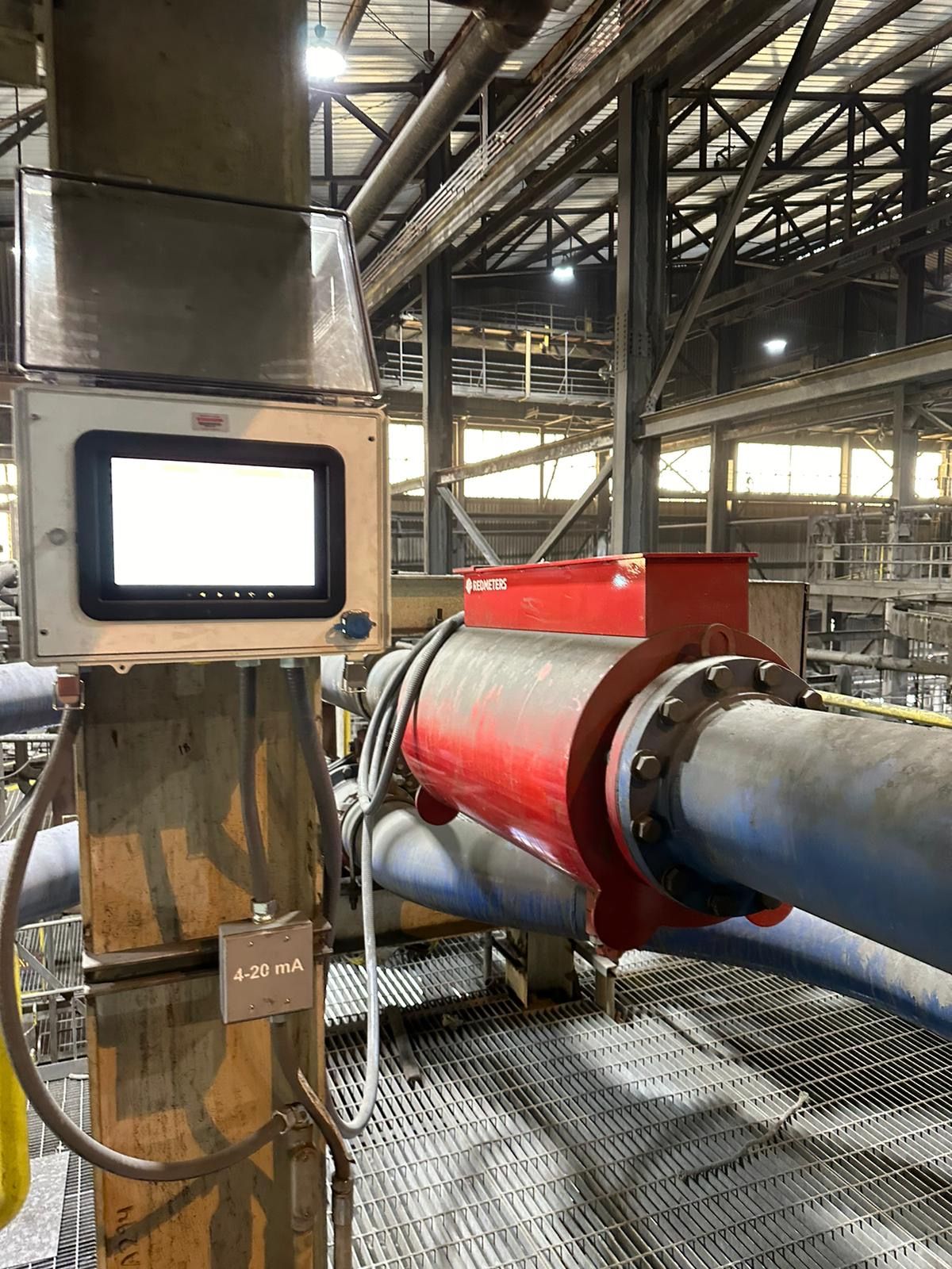 A monitoring device with a screen attached to a red pipe in an industrial setting.