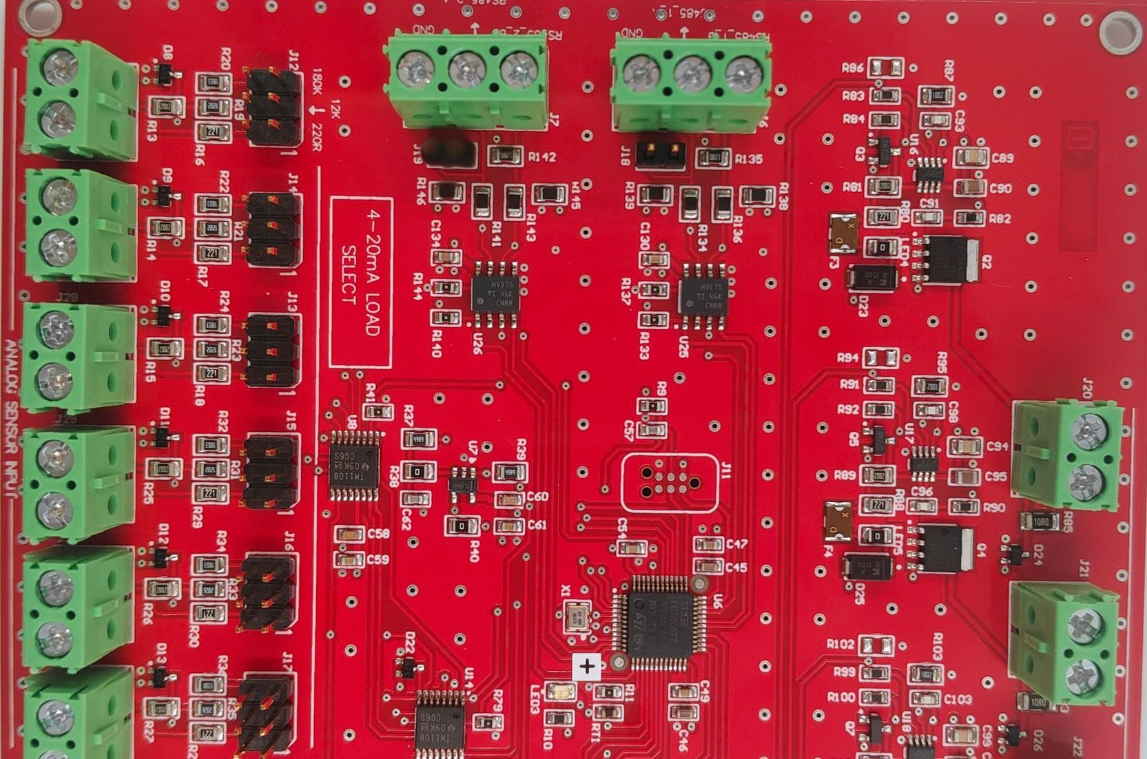 Red printed circuit board with green terminal blocks and various electronic components.