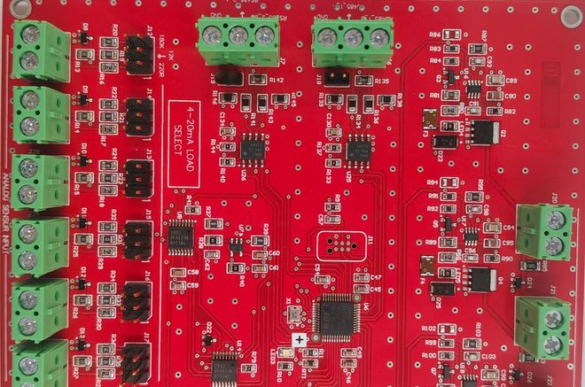 Red printed circuit board with green terminal blocks and various electronic components.