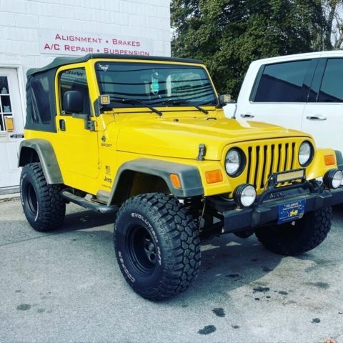Bright yellow Jeep Wrangler with lifted tires parked outside an auto shop.