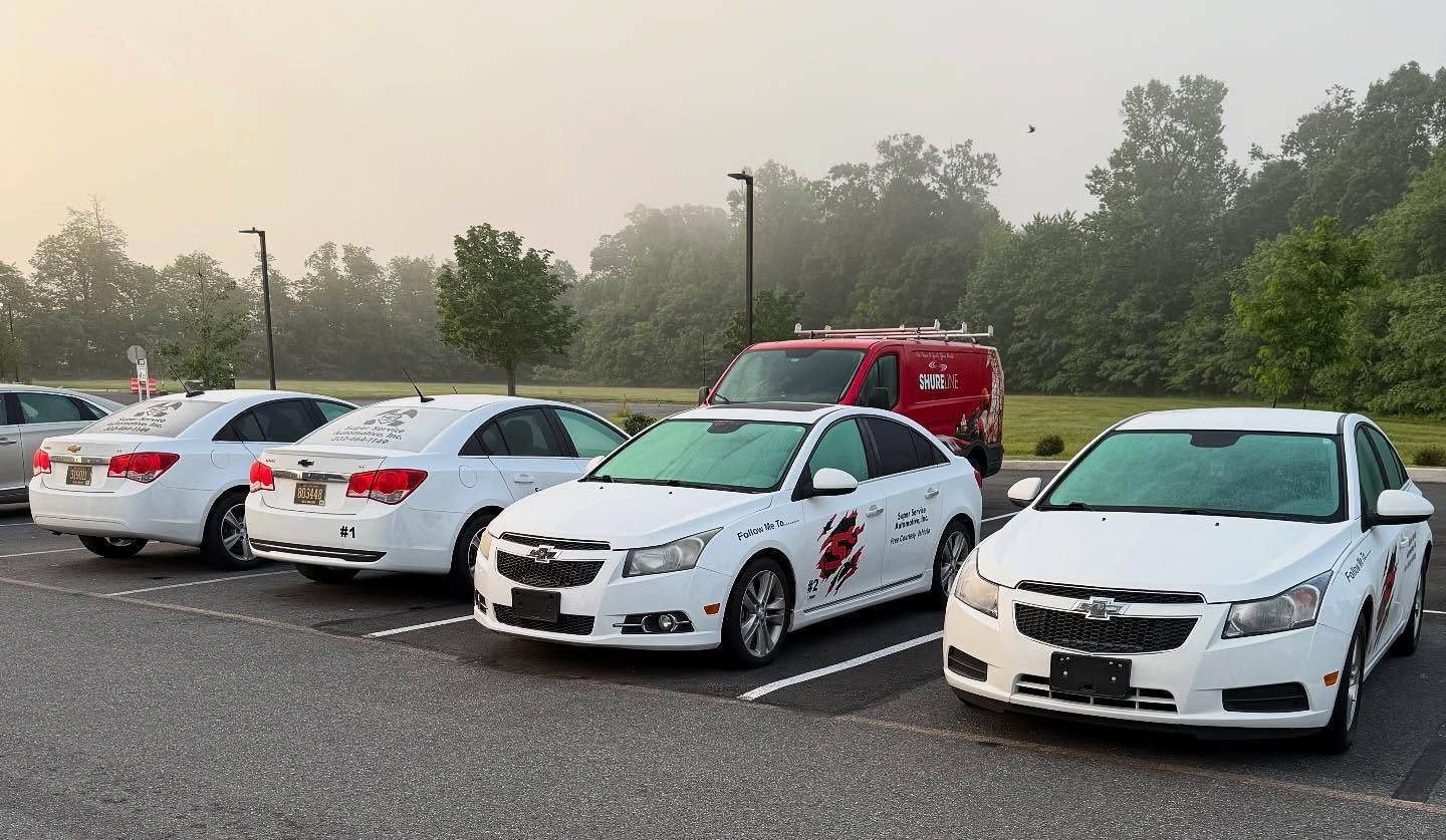 Parked white cars in a foggy lot, with a red emergency vehicle in the background.