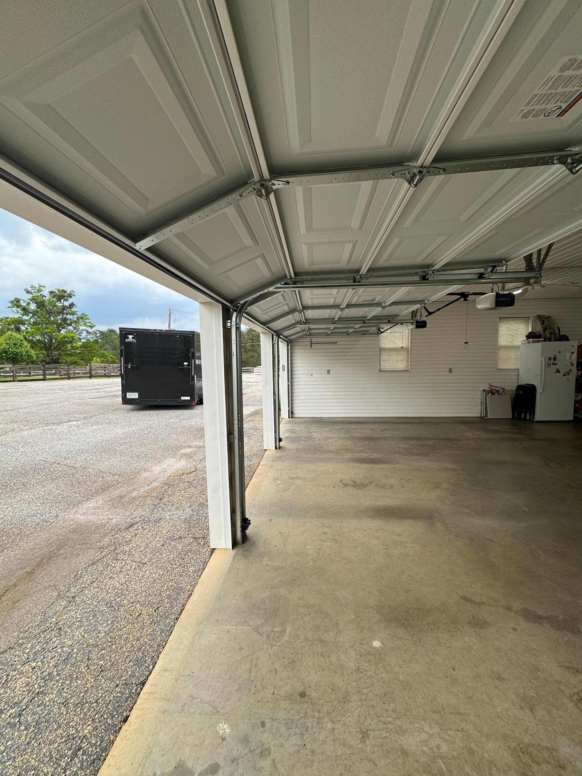 Open garage with gray concrete floor, gravel driveway, and a black vehicle in the distance.