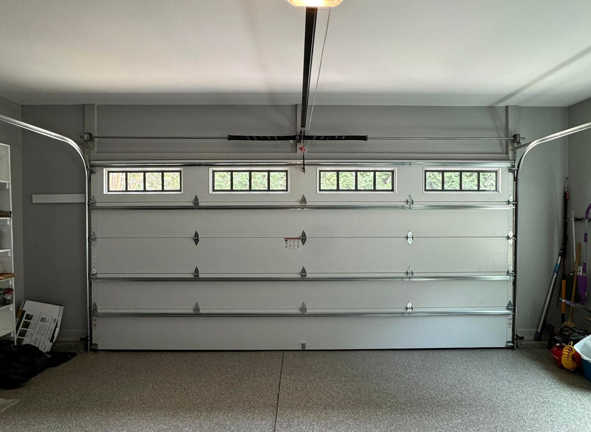 White garage door with windows, light gray walls, speckled floor, overhead opener.
