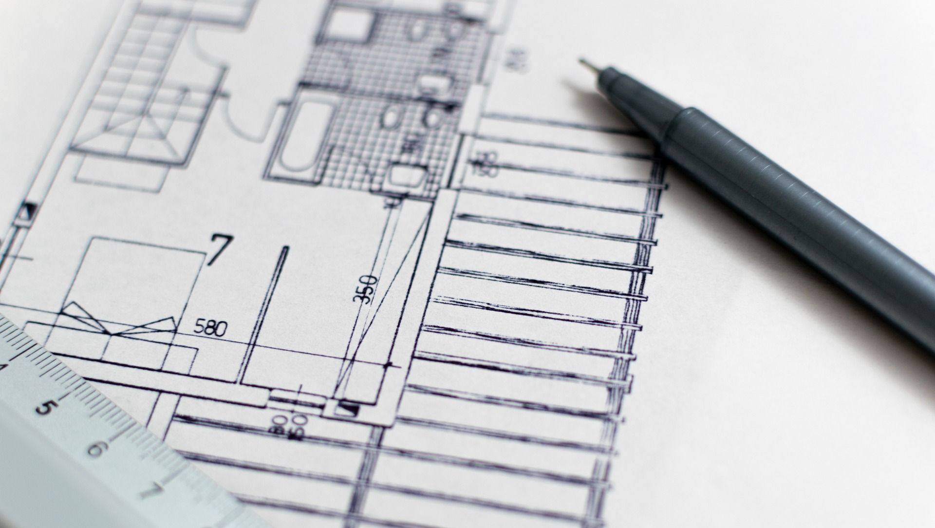 Architectural blueprints with a pen laid across the plans on a white desk.