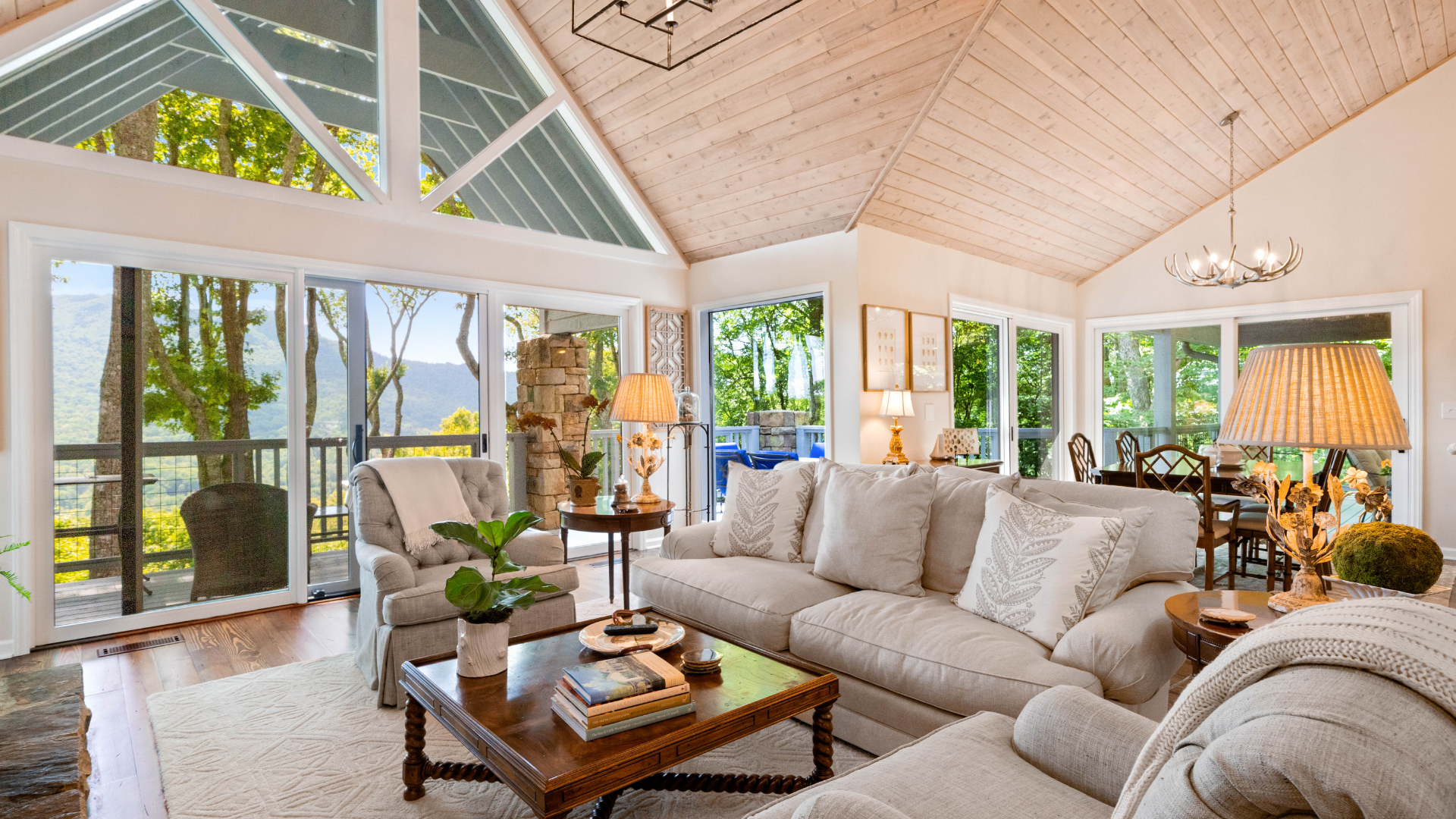Bright, airy living room with cream sofas, wooden coffee table, high vaulted ceiling, and large windows overlooking greenery