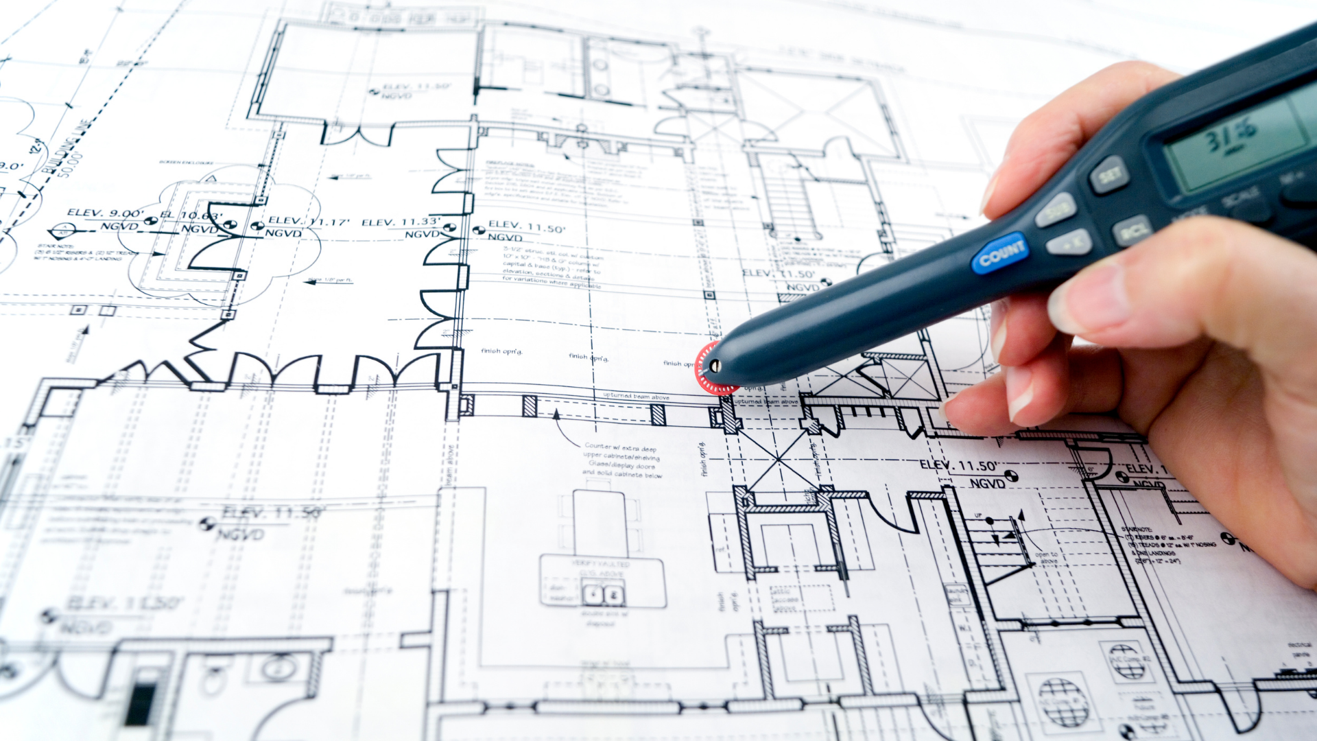 Hand holding a pen over a blue architectural floor plan, marking design details.