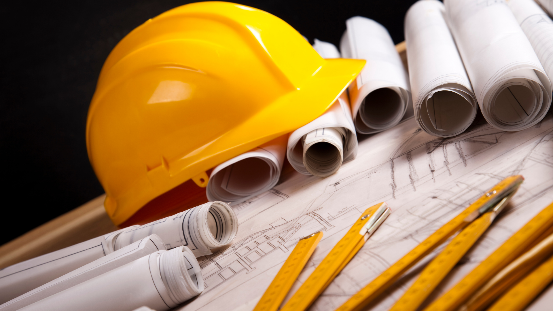 Yellow hard hat, rolled blueprints, and pencils on construction plans