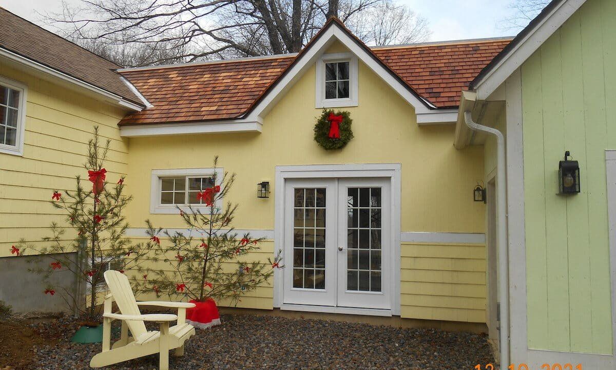 Yellow cottage courtyard with white double doors, red wreath, and a beige chair