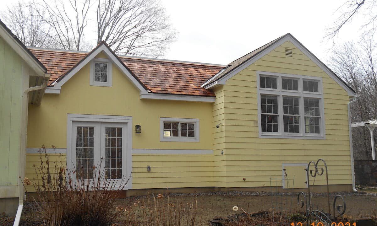 Yellow house with white-trimmed windows and a red-tiled roof in a yard on an overcast day