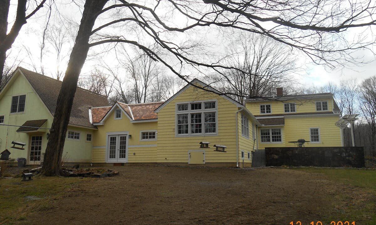 Yellow house with multiple gables and bare trees in front on a cloudy day