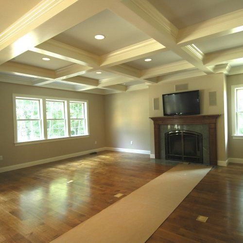 Empty living room with hardwood floors, coffered ceiling, fireplace, and large windows