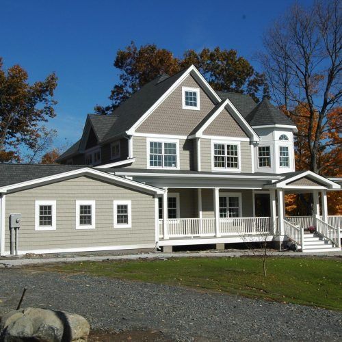 Large gray two-story house with white trim, front porch, and attached garage on a sunny day