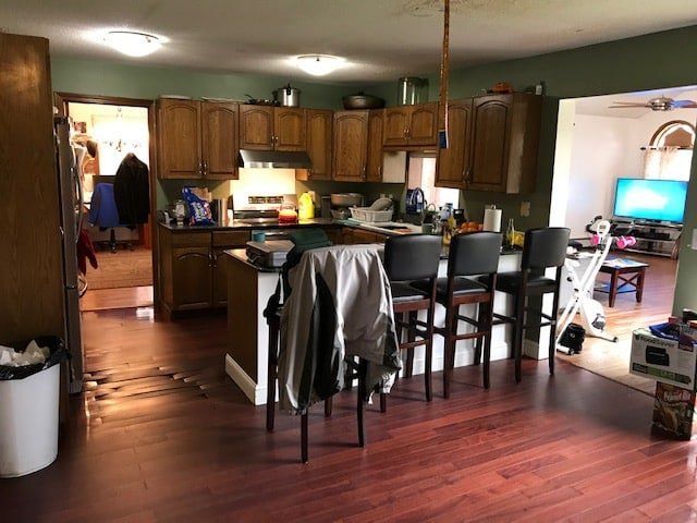 Kitchen and dining area with wooden cabinets, island, barstools, and a living room visible beyond the doorway