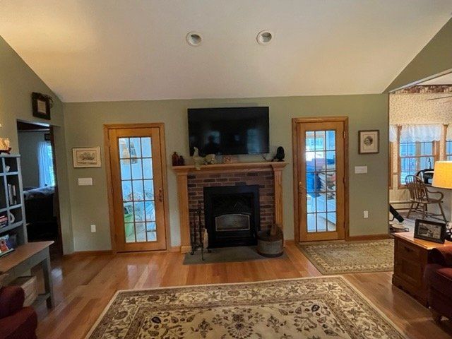 Living room with brick fireplace, TV, hardwood floors, and French doors on either side