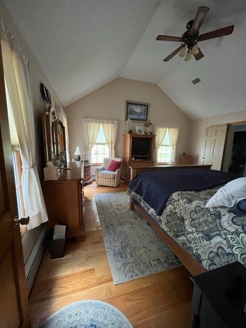 Bedroom with vaulted ceiling, bed, fireplace, rug, and two windows with curtains
