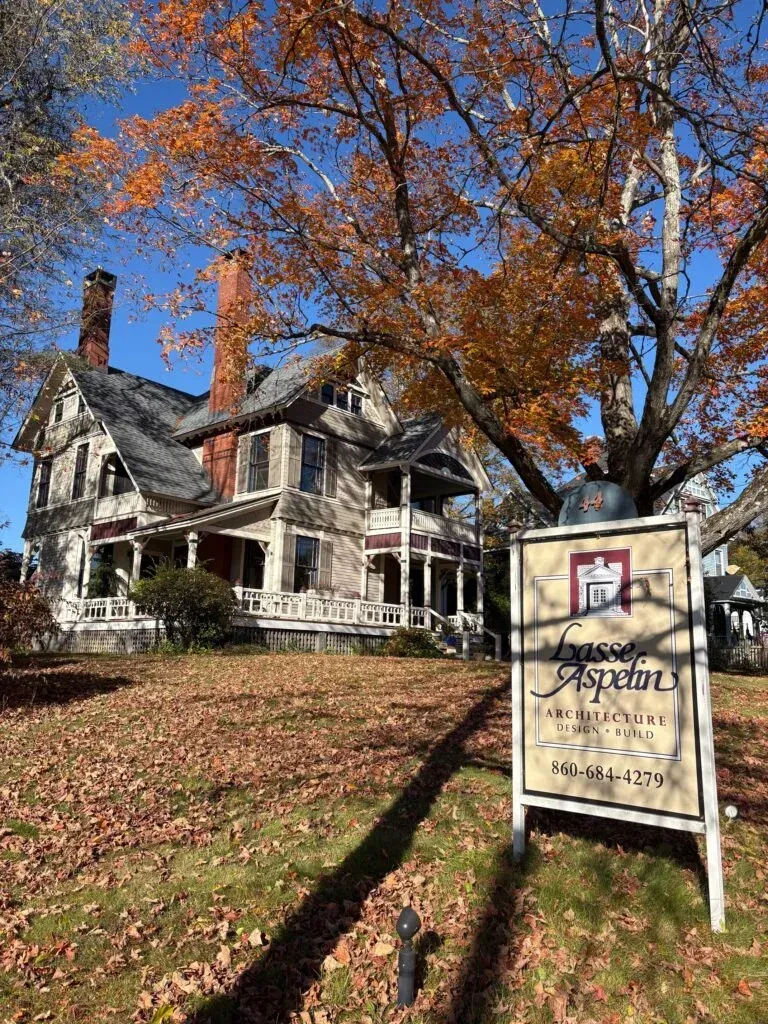 Historic white Victorian house with autumn trees and a sign in front on a sunny day