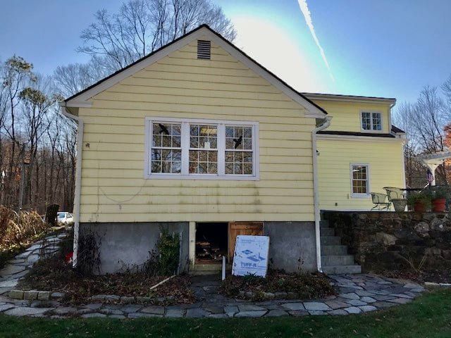 Yellow house with white trim and stone steps, viewed from the back yard on a sunny day