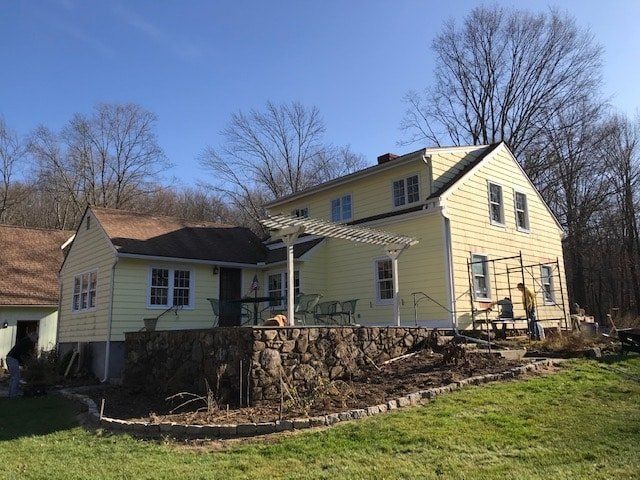 Yellow house with stone retaining wall on a wooded hillside under a clear blue sky