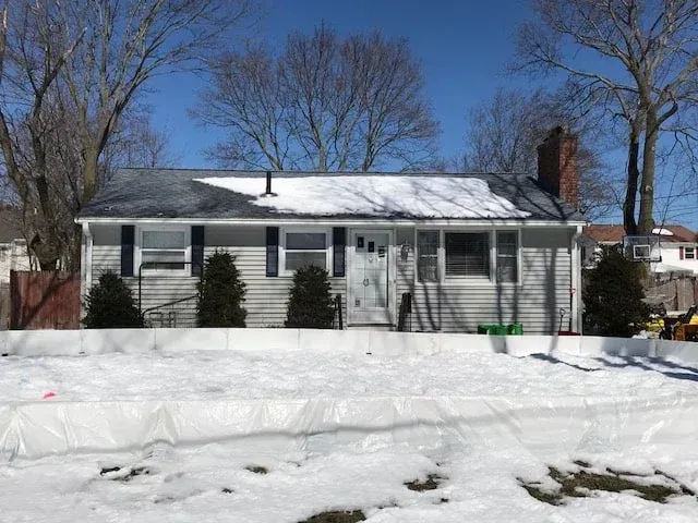 Snow-covered house with bare trees and a brick chimney on a clear winter day