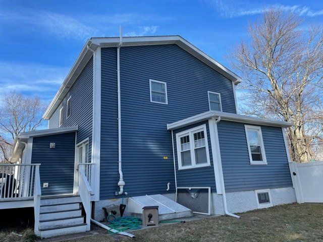 Blue two-story house with white trim, small porch, and basement entrance under a clear sky
