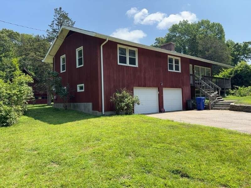 Red house with white garage doors, front steps, and a large green lawn under a blue sky.