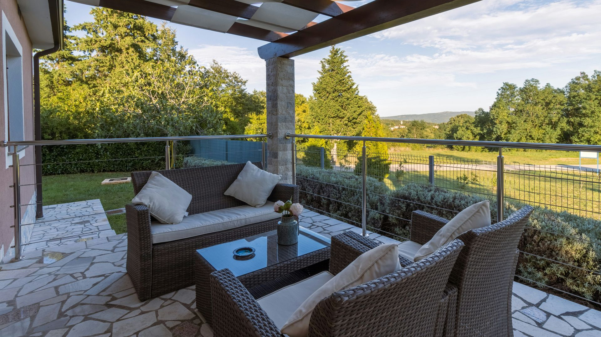 Covered patio with wicker seating, glass coffee table, and a scenic view of green hills