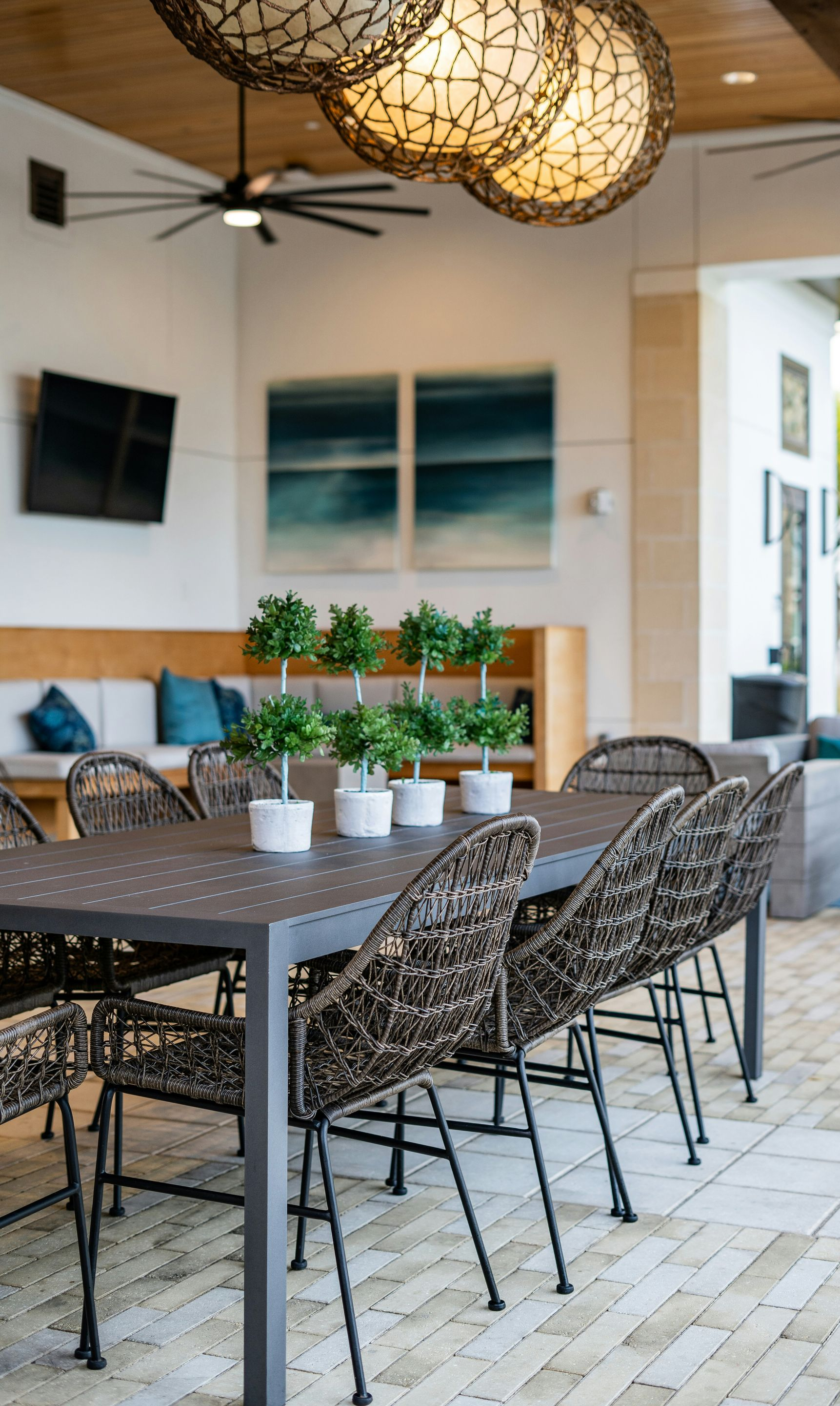 Open-air patio dining area with woven chairs, gray tables, potted plants, and hanging lights