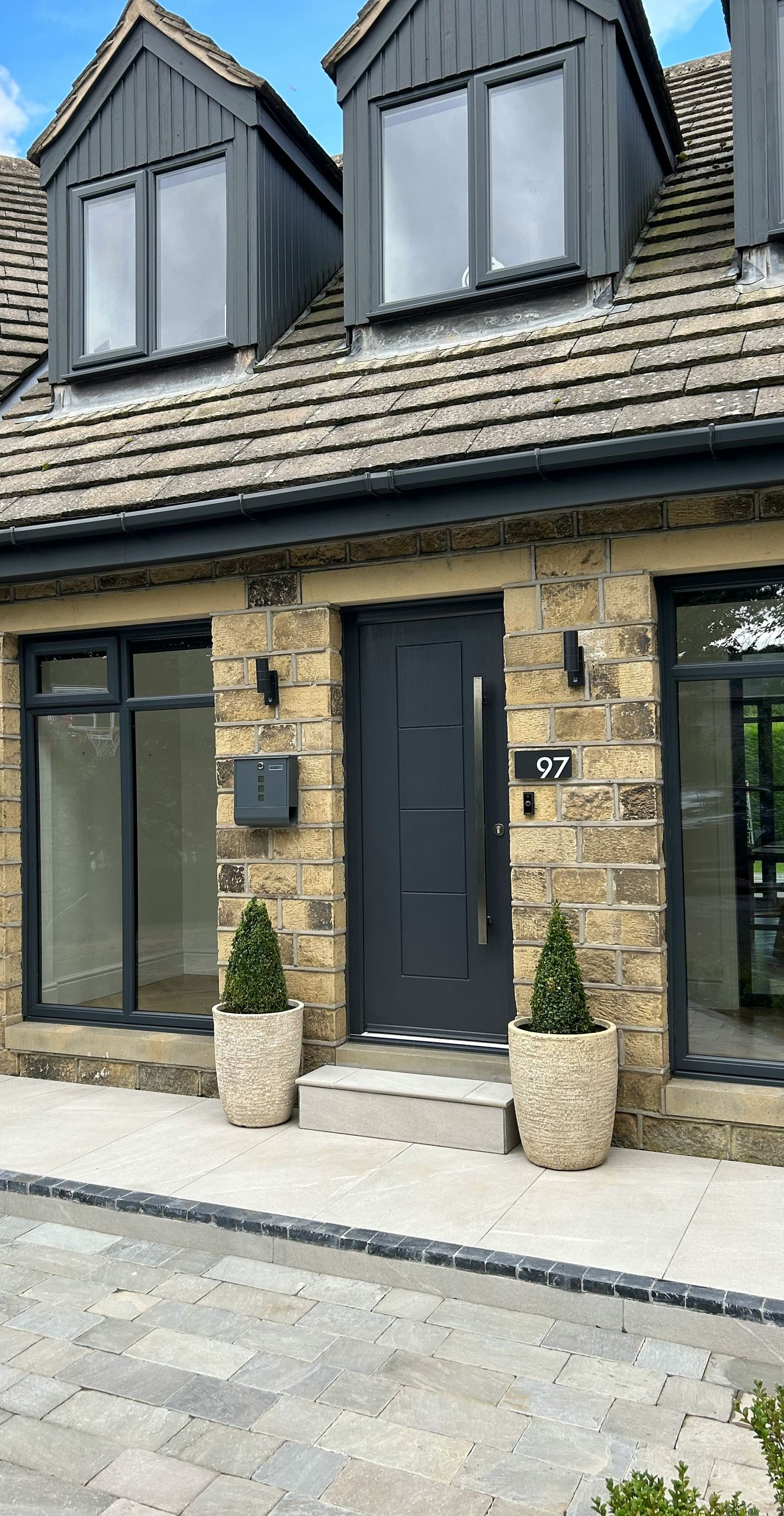 Stone townhouse facade with black door, dormer windows, and potted plants by the entrance
