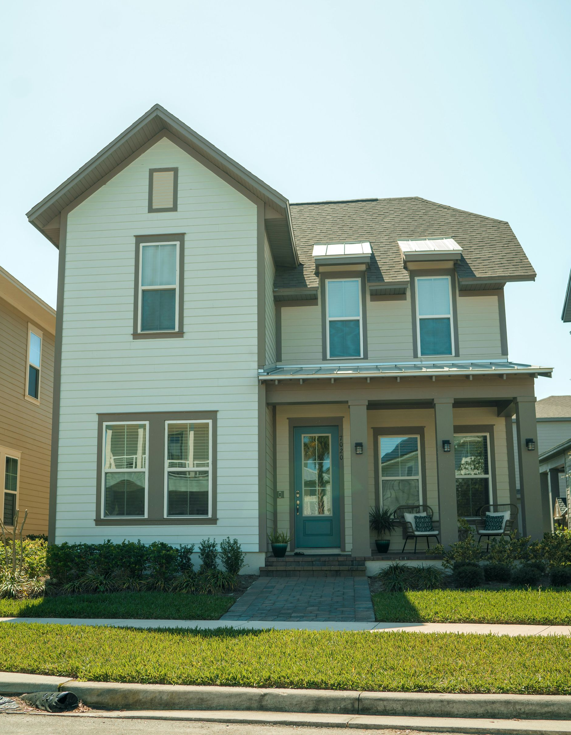 Two-story white house with a front porch, teal door, and trimmed lawn under a clear sky