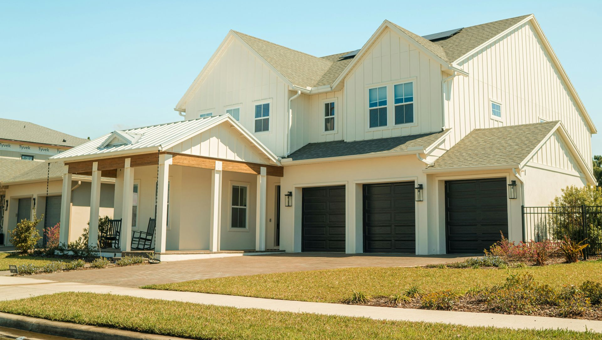 Suburban two-story white house with a covered front porch and three-car garage under a clear sky