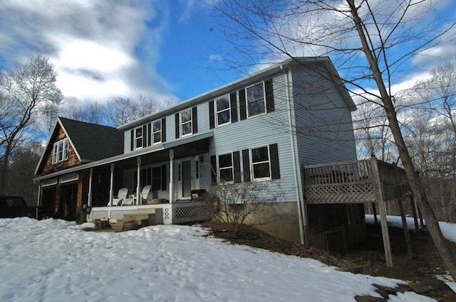Snow-covered two-story blue house with a porch under a cloudy sky