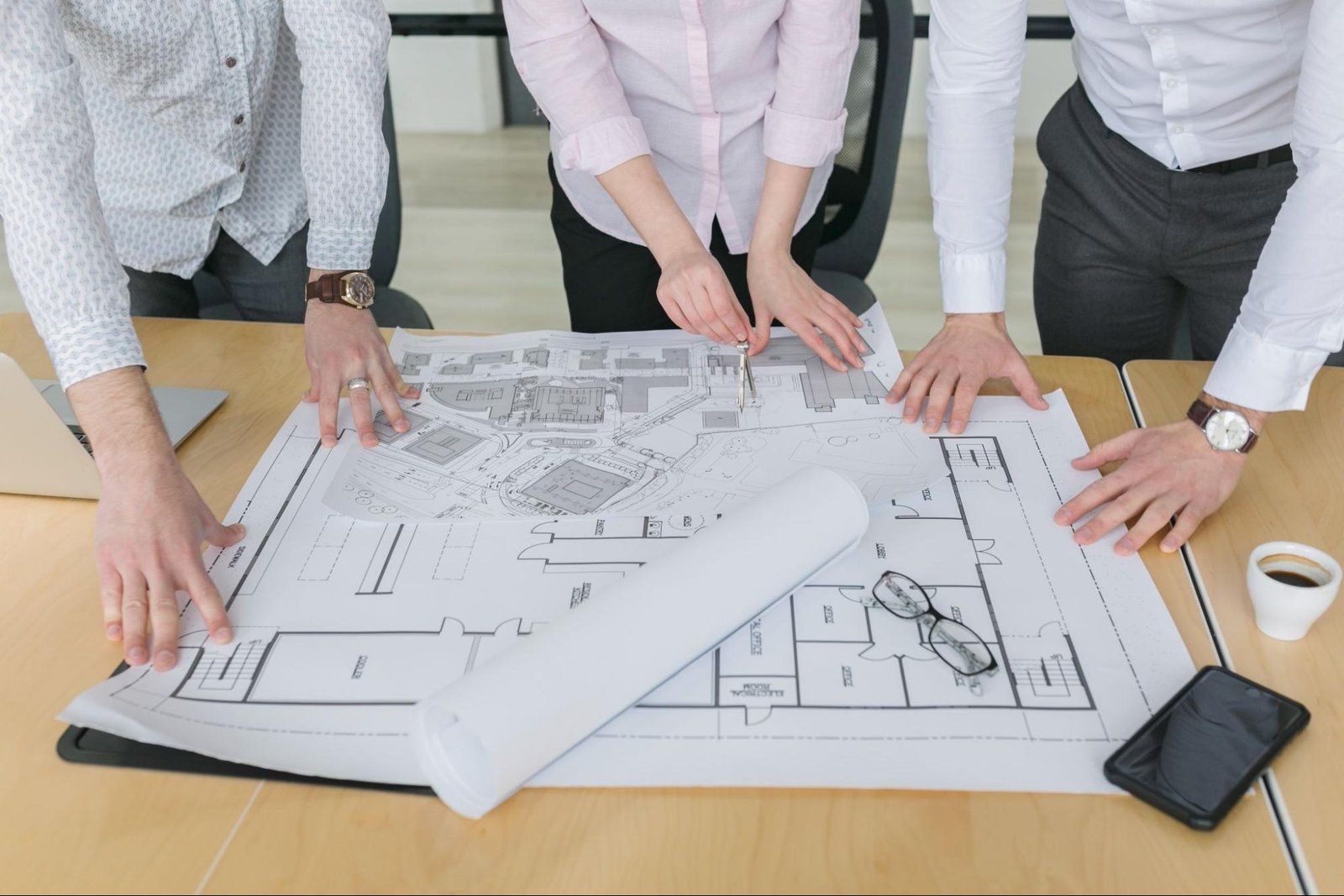 People reviewing architectural blueprints on a table with rolled plans and a smartphone nearby