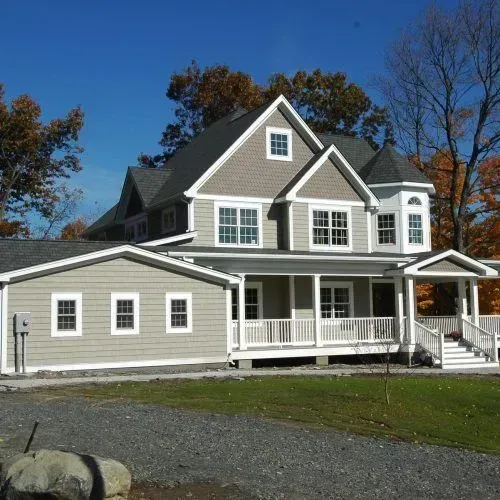 Large gray two-story house with white trim and porch in a sunny suburban yard