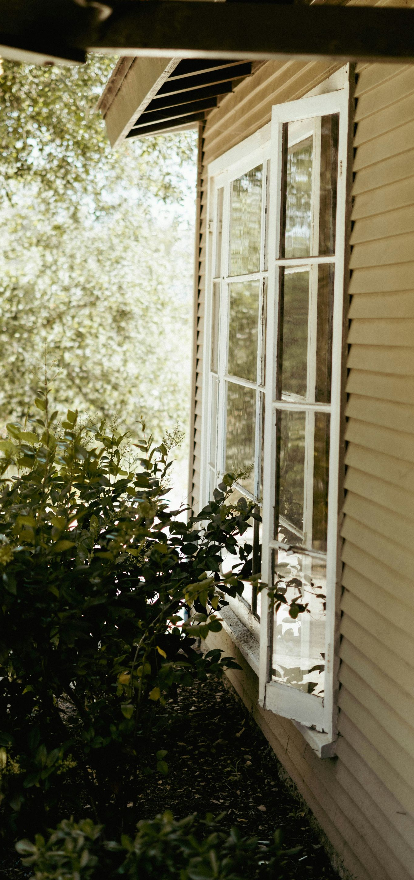 White house exterior with open French doors beside a leafy garden and covered porch