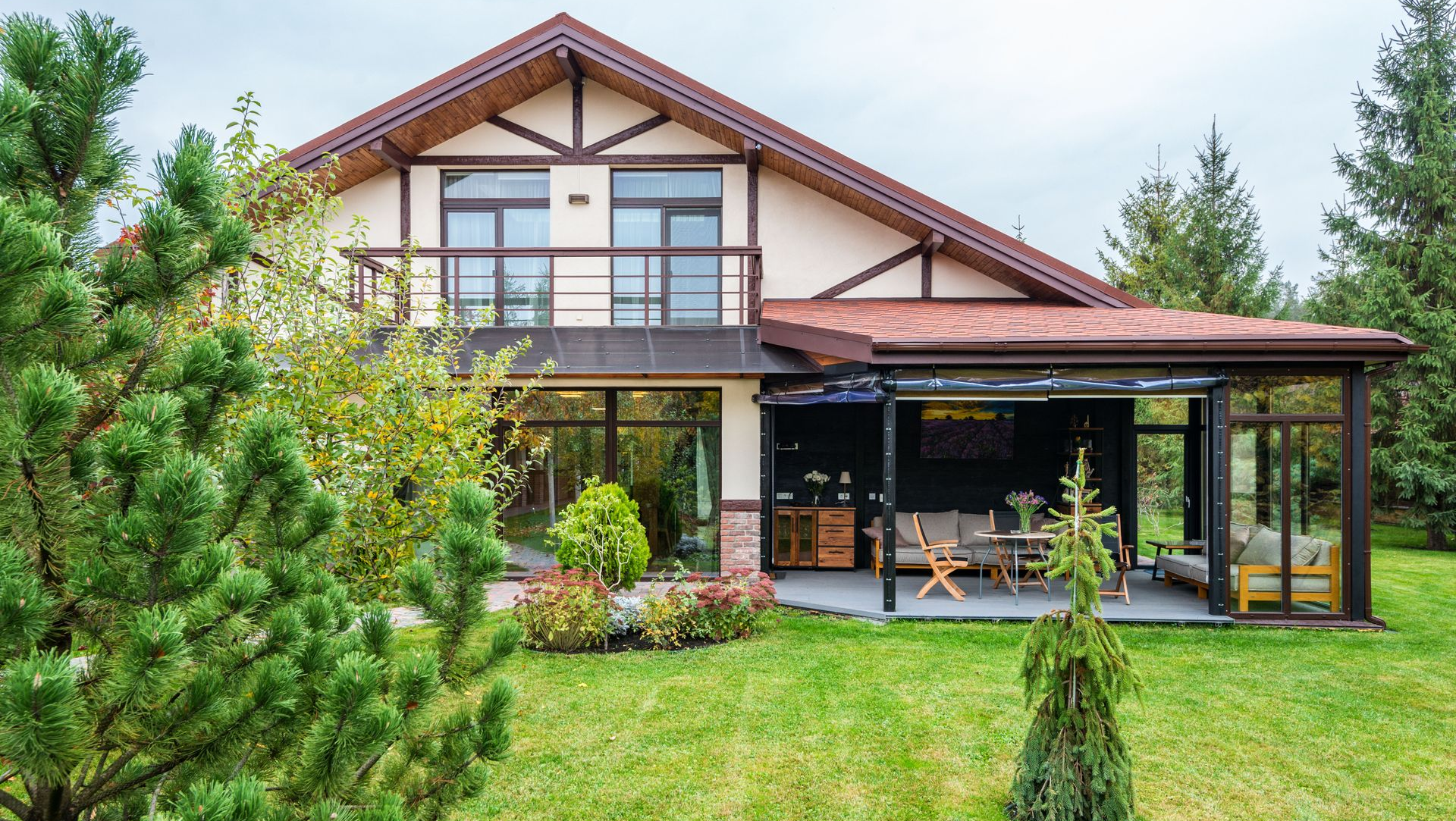Modern house with a red roof, covered patio, and lush green lawn surrounded by trees.