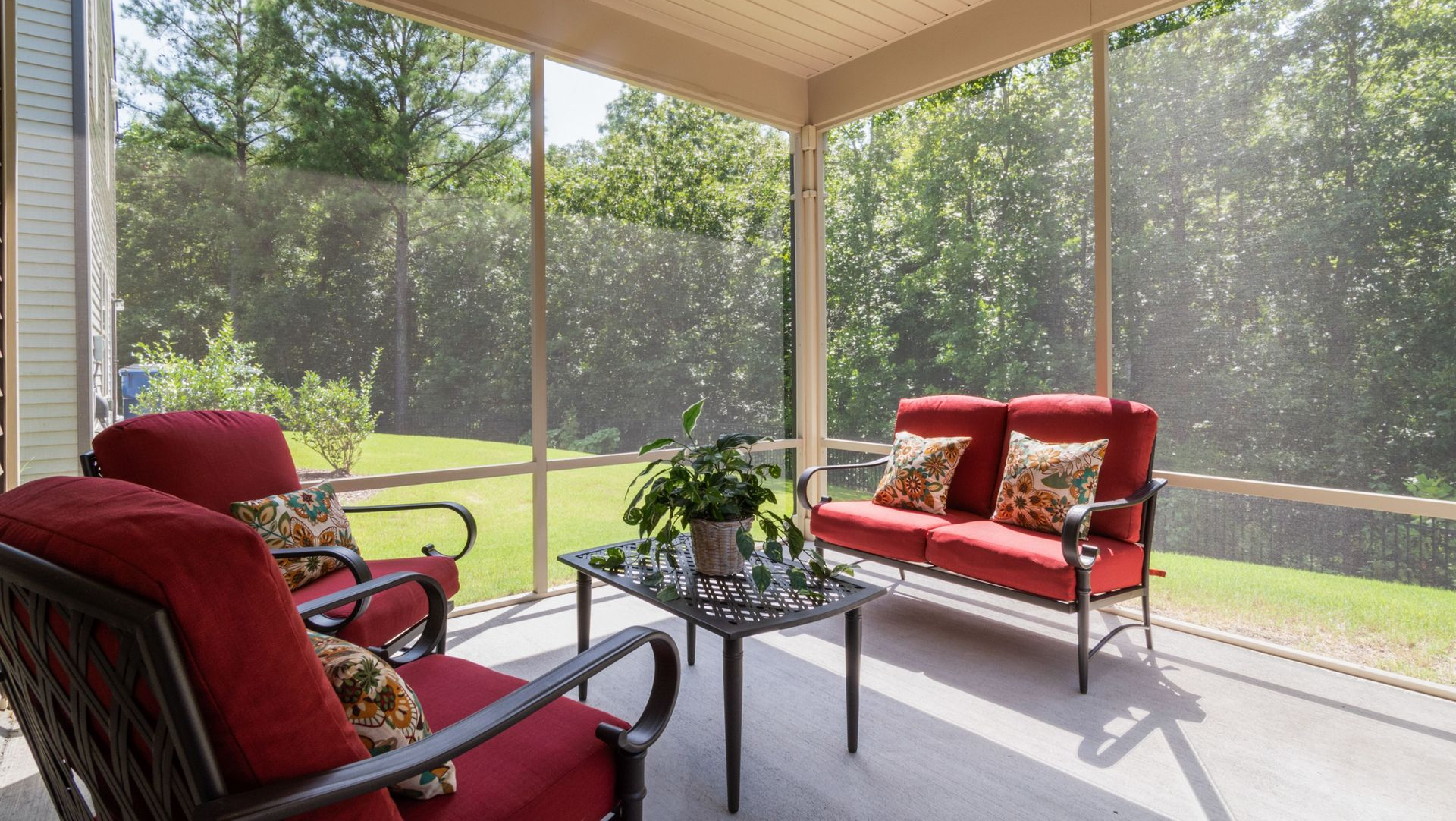 Screened porch with red cushioned seating, coffee table, and view of a green backyard.