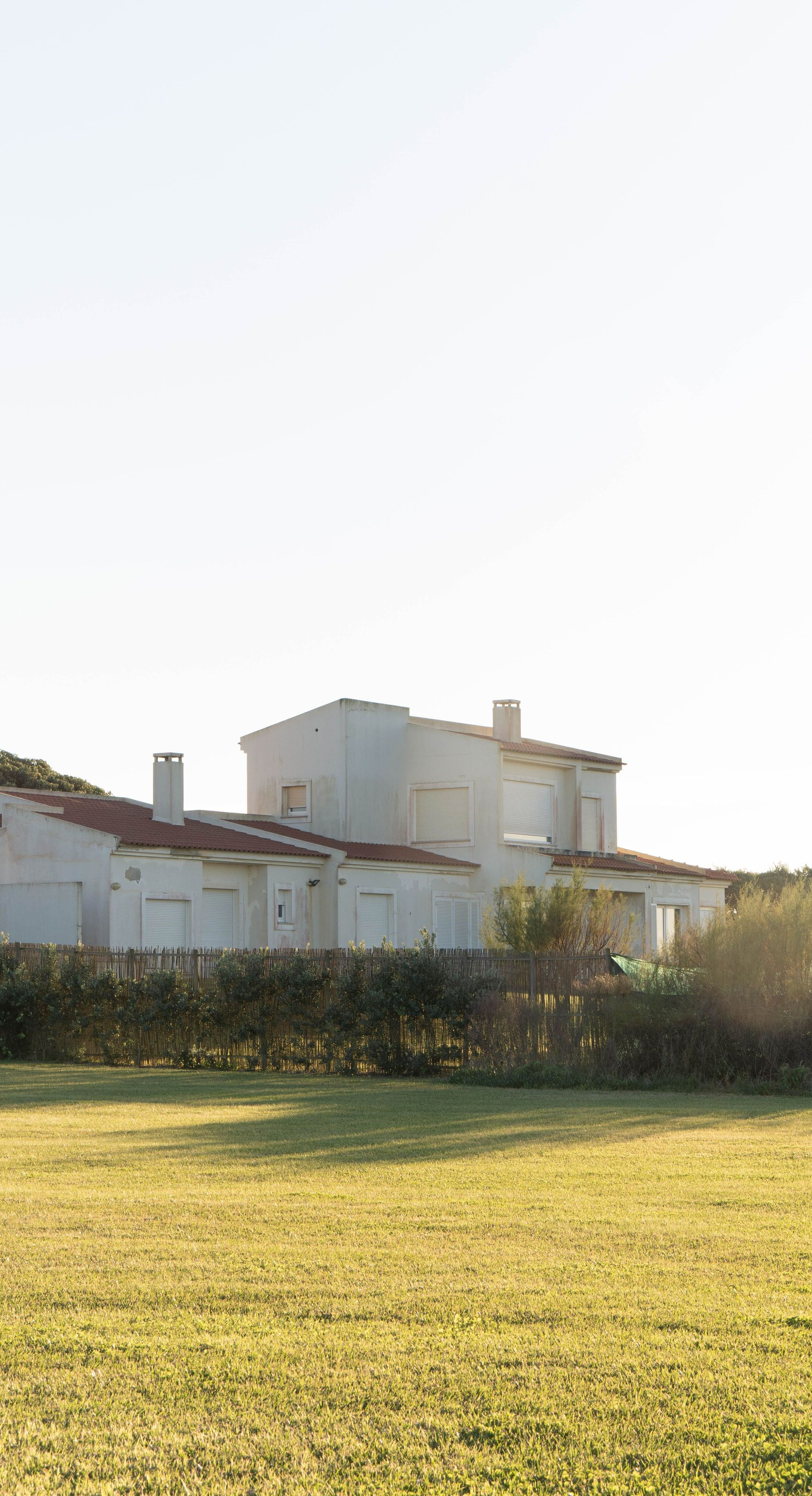 Modern white house behind a grassy field under a bright sky