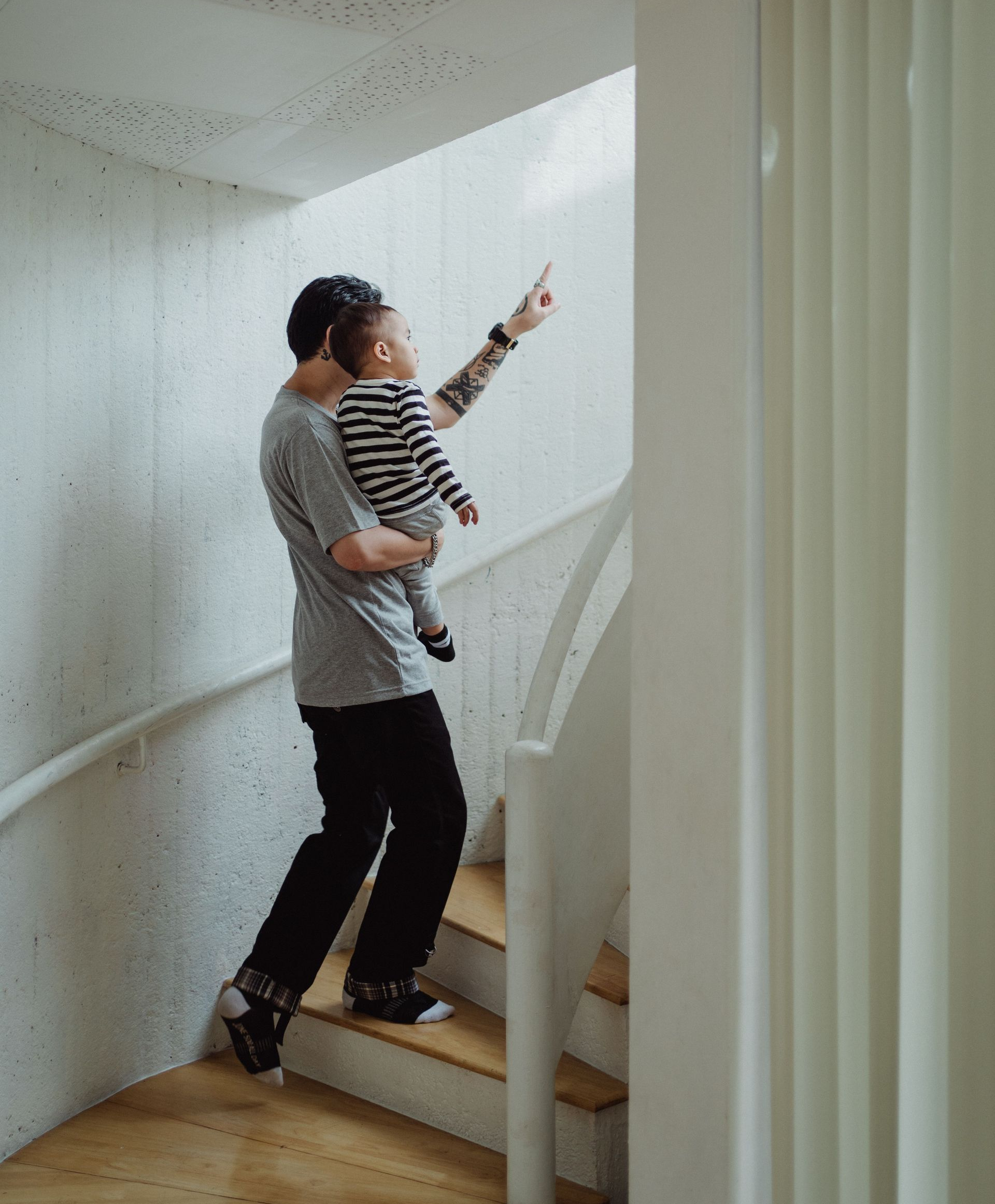 Adult carrying a child up a staircase and pointing ahead in a bright hallway