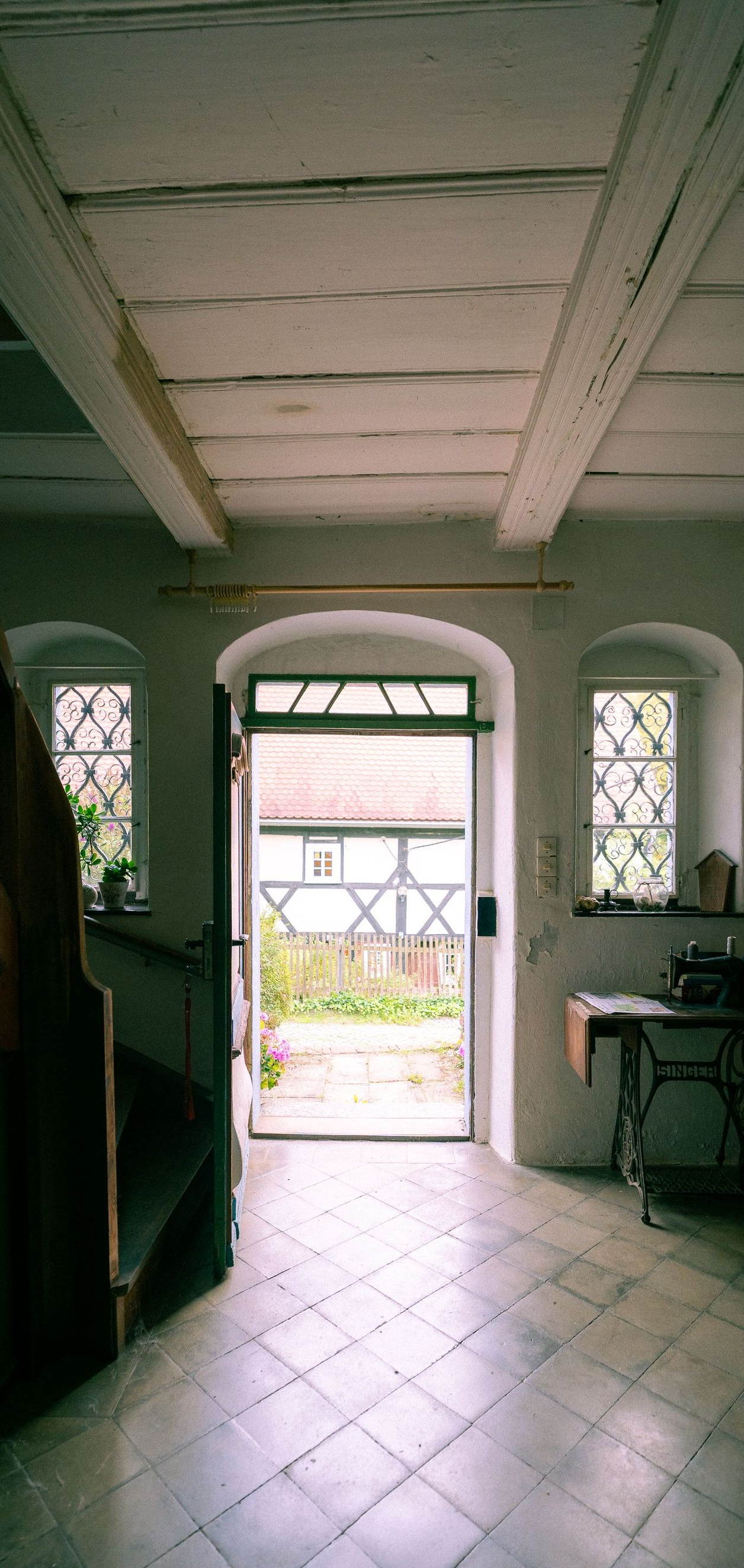 Open front doorway with tiled floor and arched windows, looking out to a bright garden path