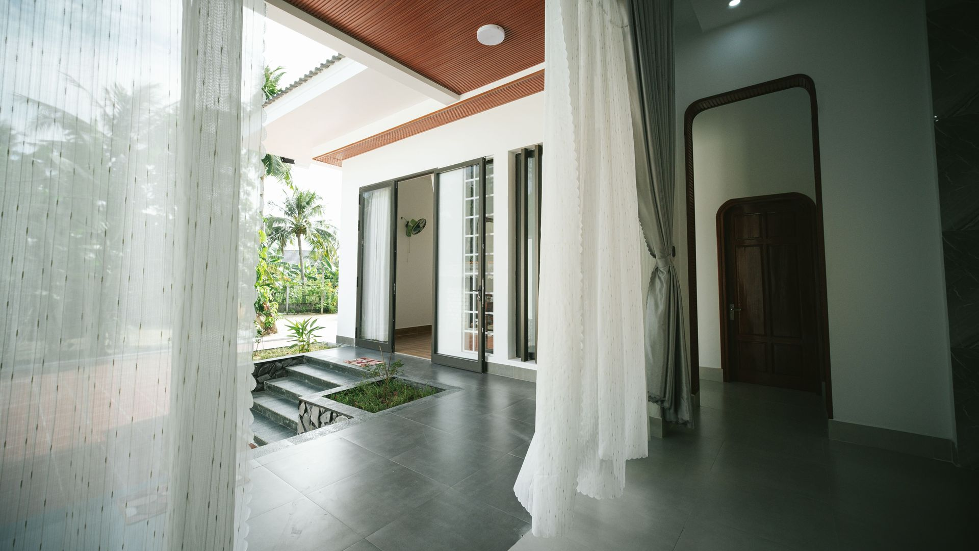 Modern porch with sheer curtains, wooden ceiling, potted plants, and open doors leading inside