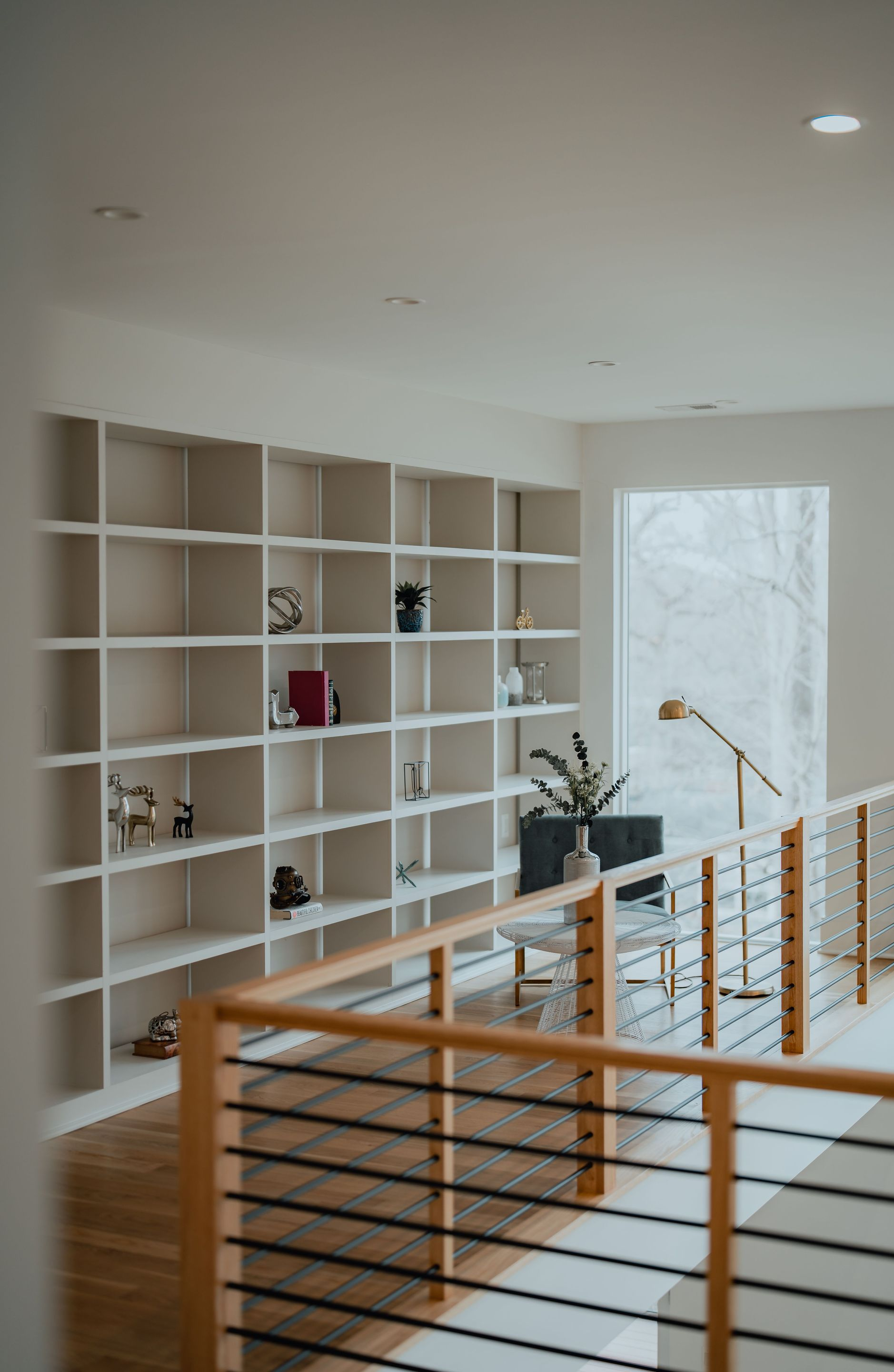 Bright modern loft with white shelving, wooden railing, and large window overlooking snowy trees
