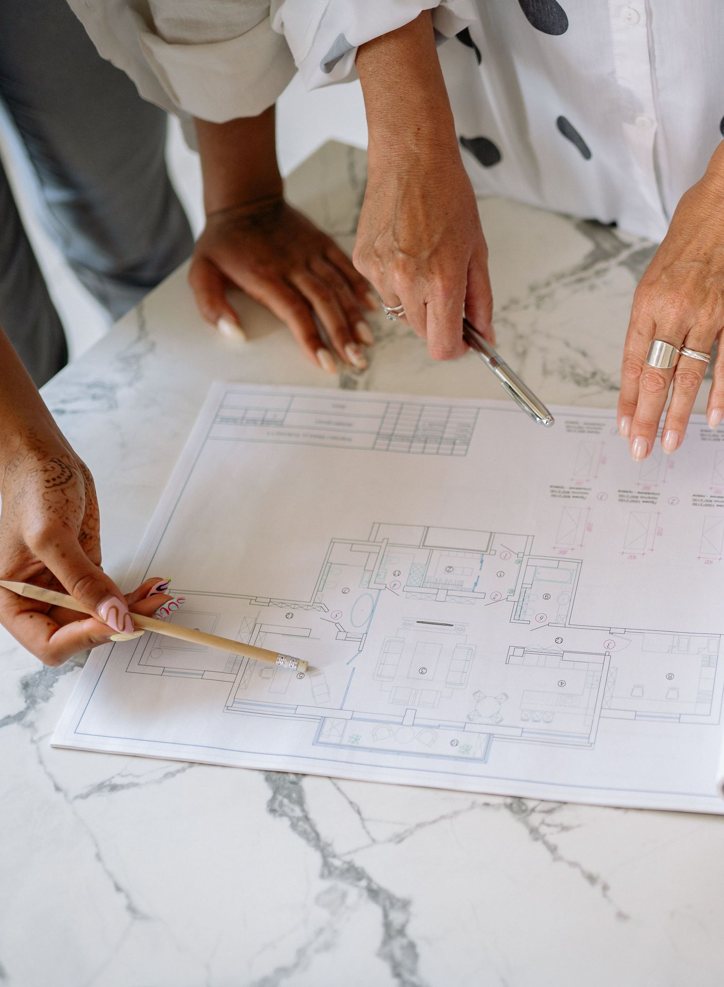 Hands with pencils reviewing a floor plan on a marble table