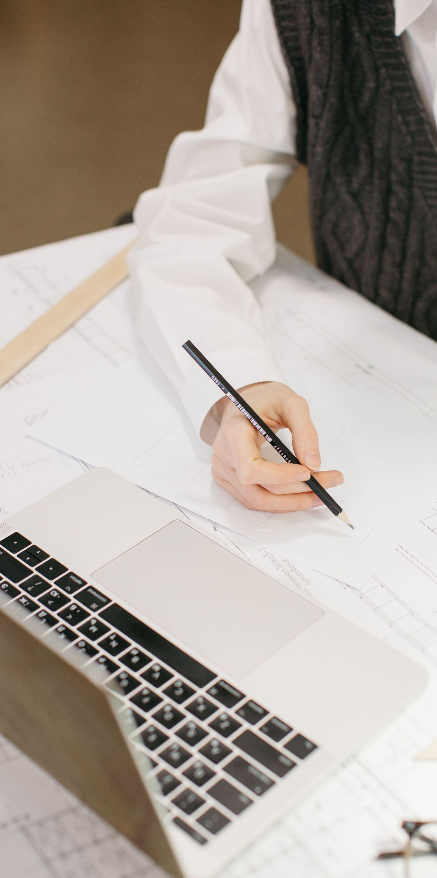 Person writing on paper beside a laptop at a desk