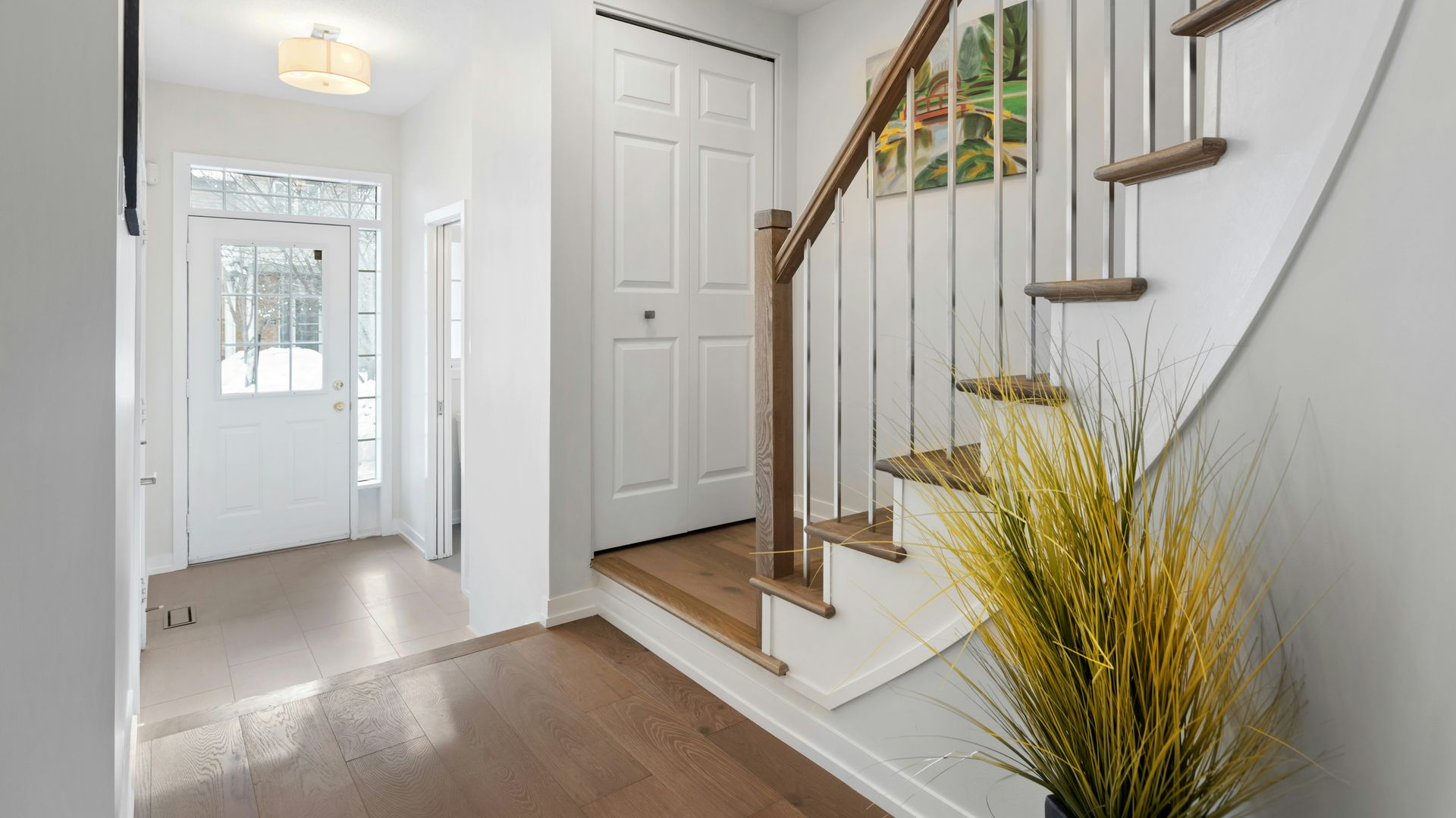 Bright entryway with white walls, wood staircase, and a potted plant near the stairs.