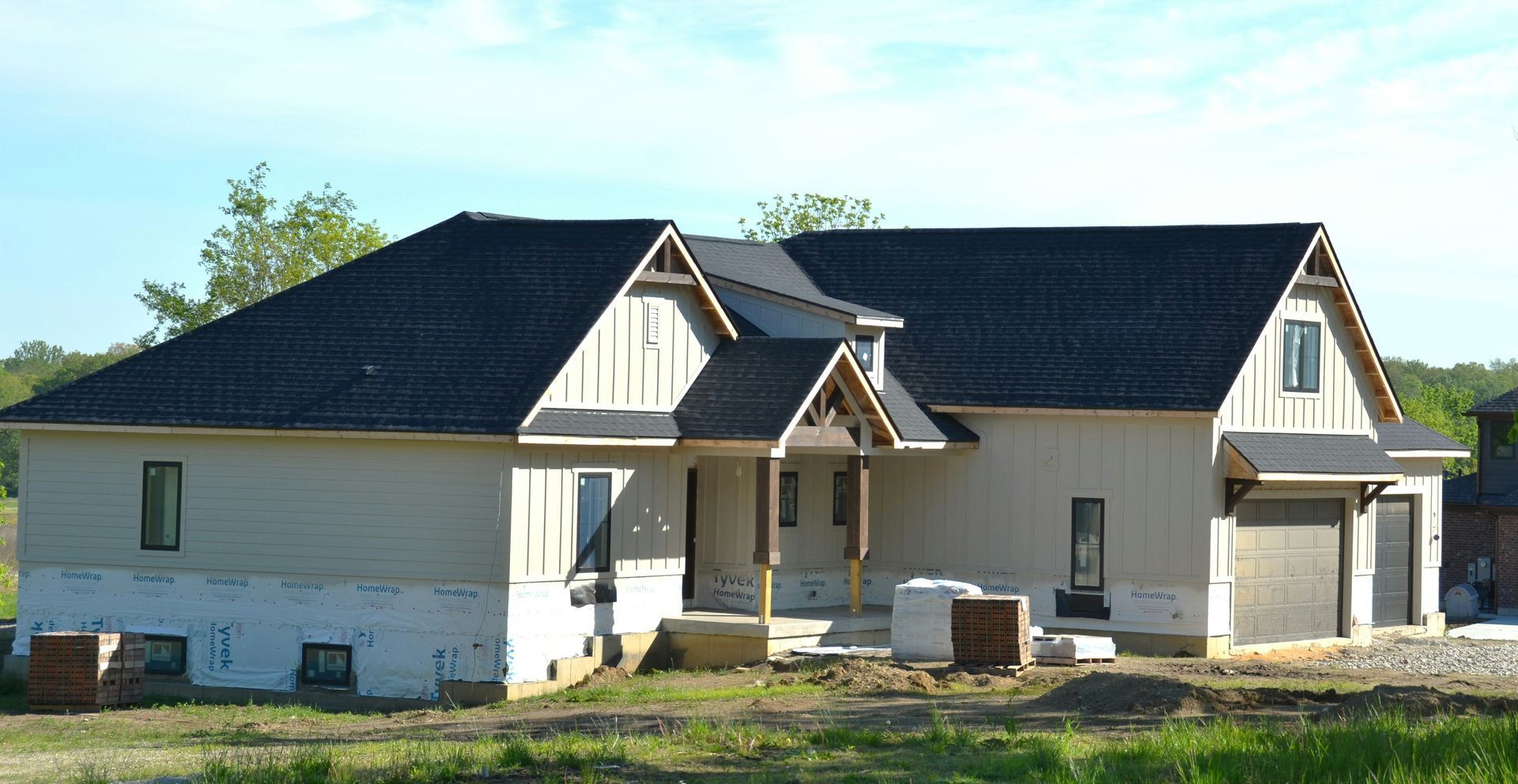 New house under construction with beige siding, dark roof, and a covered front porch