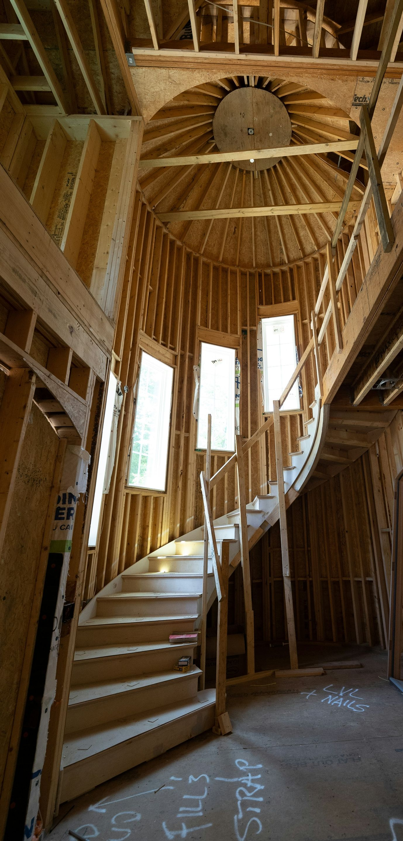 Curved wooden staircase inside a timber-framed building with tall windows and exposed beams